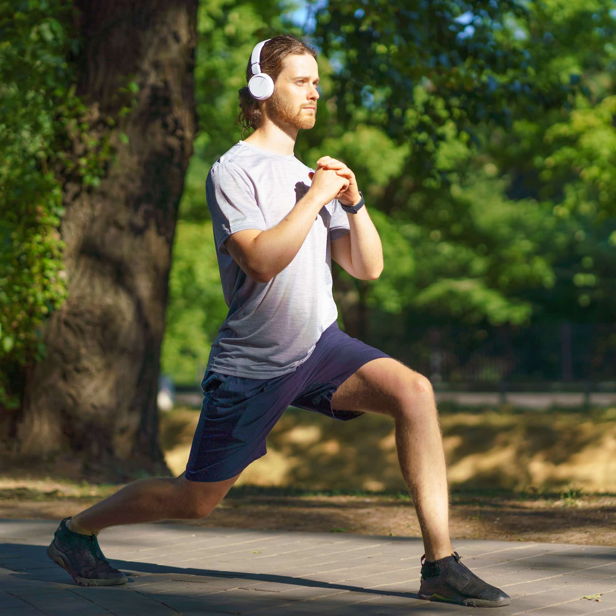 Young male sportsman in headphones doing sports exercises lunges outdoors